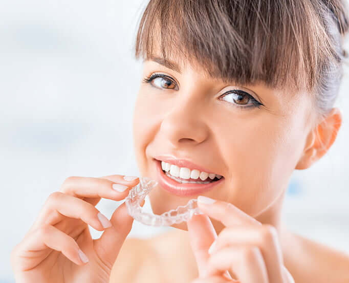 woman inserting clear aligners onto her teeth